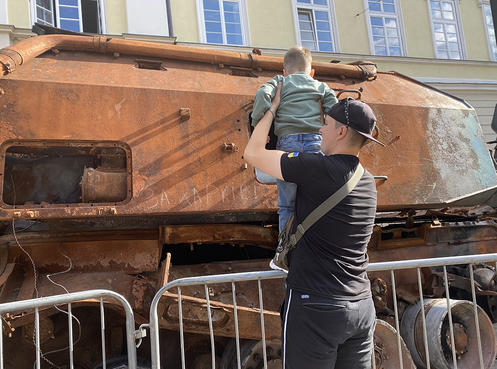 A child gets some help to look at what's left of a Russian tank Sept. 2, 2022 in Rynok Square in Lviv, Ukraine. It was part of a display of tanks and other Russian equipment destroyed by Ukraine's armed forces in the conflict that began Feb. 24, 2022. (Rhina Guidos)