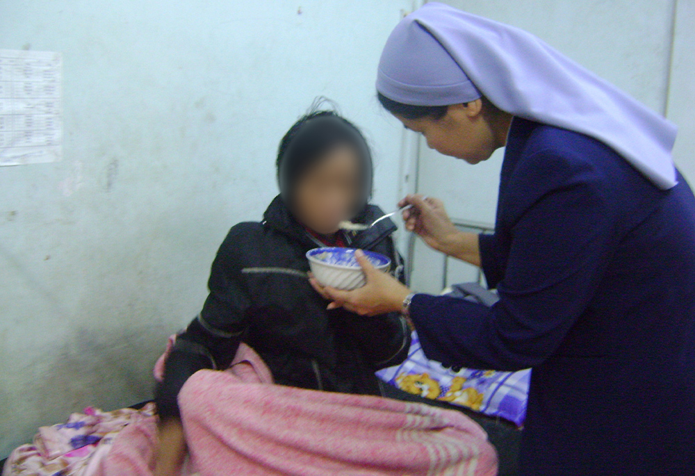 Filles de Marie Immaculée Sr. Agnes Truong Ngoc Lan feeds a seriously ill patient (face obscured to protect identity) Dec. 3, 2022, in Hue. (GSR photo/Joachim Pham)