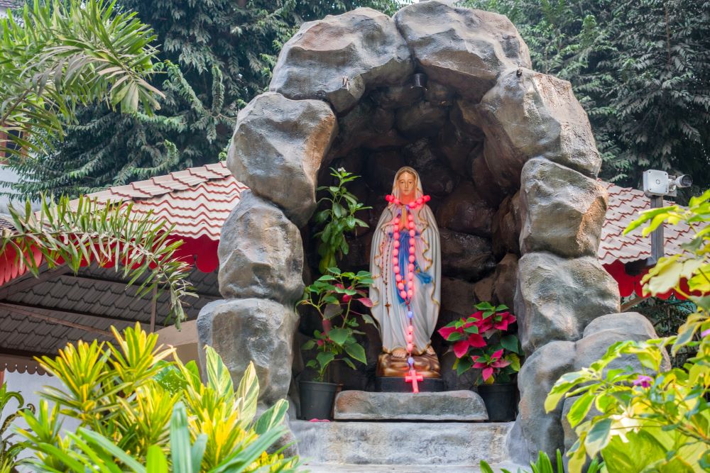 Statue of Mother Mary under stone arch in a garden