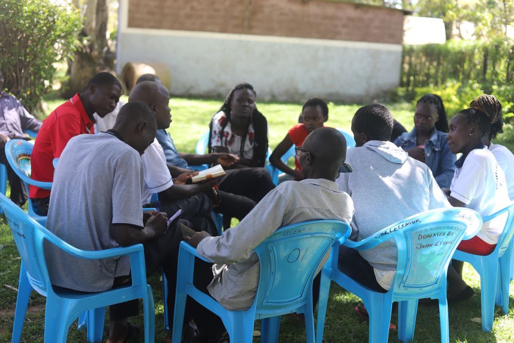 A group of young people sit in blue chairs and talk.