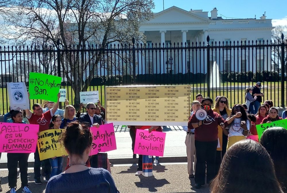 Protesters stand with signs outside fence in front of White House.