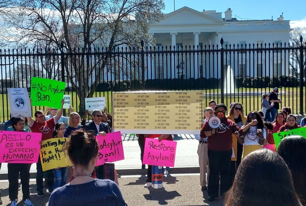 Protesters stand with signs outside fence in front of White House.