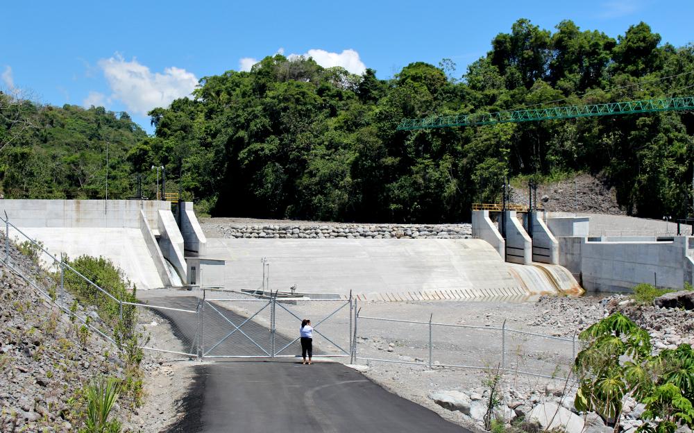 Un muro de concreto muy alto, la represa La Cuchilla, detiene el agua del río en una zona boscosa. 