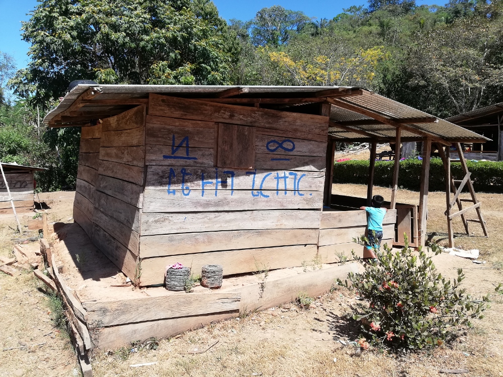 Una vivienda humilde de madera con un mensaje reivindicativo de la lengua ngäbe escrito en sus paredes externas.
