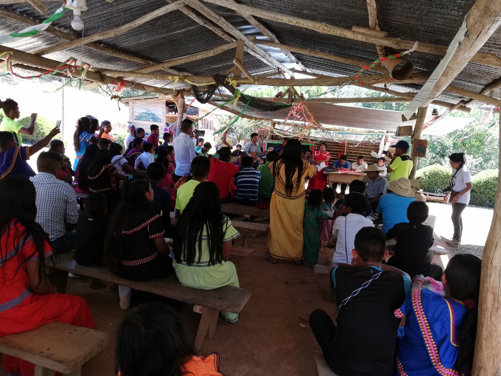 An assembly of indigenous representatives gathered under a bohío or thatched roof with corrugated metal sheets.