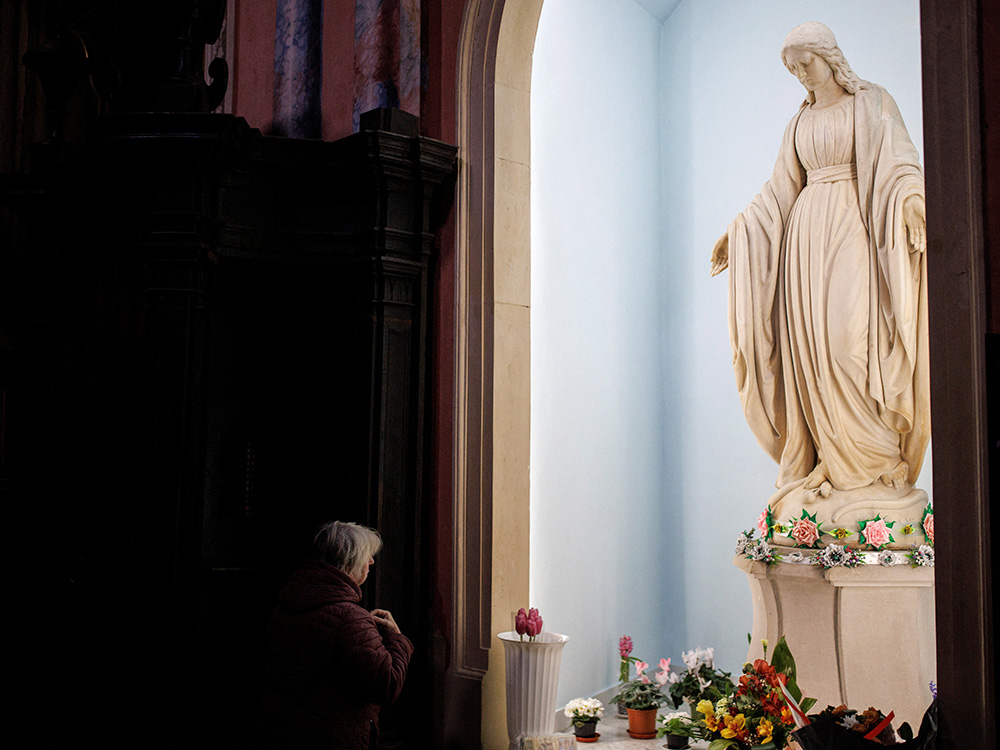A woman prays in front of a statue of Mary on March 29, 2022, inside Bernardine Monastery in Lviv, Ukraine. (CNS/Reuters/Alkis Konstantinidis)