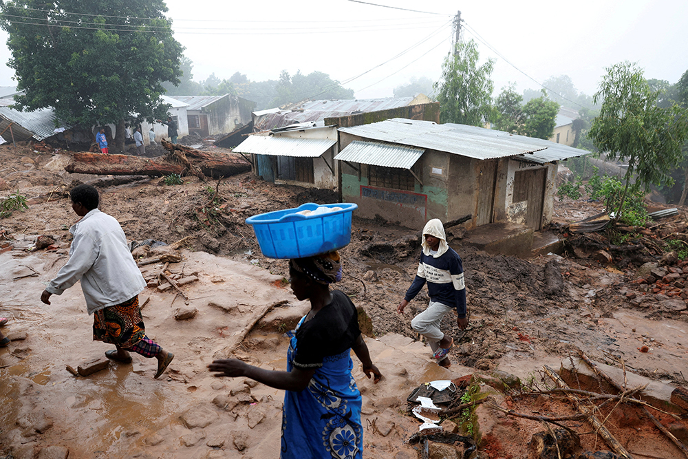 People walk through mud in a damaged residential area
