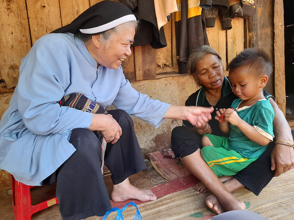 Mary Queen of Peace Sr. Teresa Nguyen Thi Bich offers candy to a grandchild of Mary Ly at her dilapidated house in the Vietnam Central Highlands. The Se Dang ethnic woman, 65, has 12 children who grow rice and coffee for a living. (Joachim Pham)