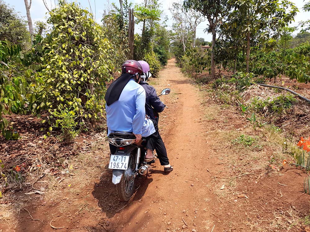 Two sisters travel by motorbike on a narrow path through coffee farms to visit ethnic villagers in Kon H'ring Parish in Cu M'gar district of Dak Lak province in Vietnam. (Joachim Pham)