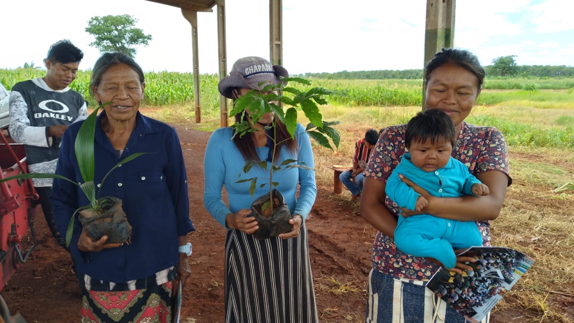 Three Indigenous people of the Guarani-Kaiowa peoples pose with saplings 