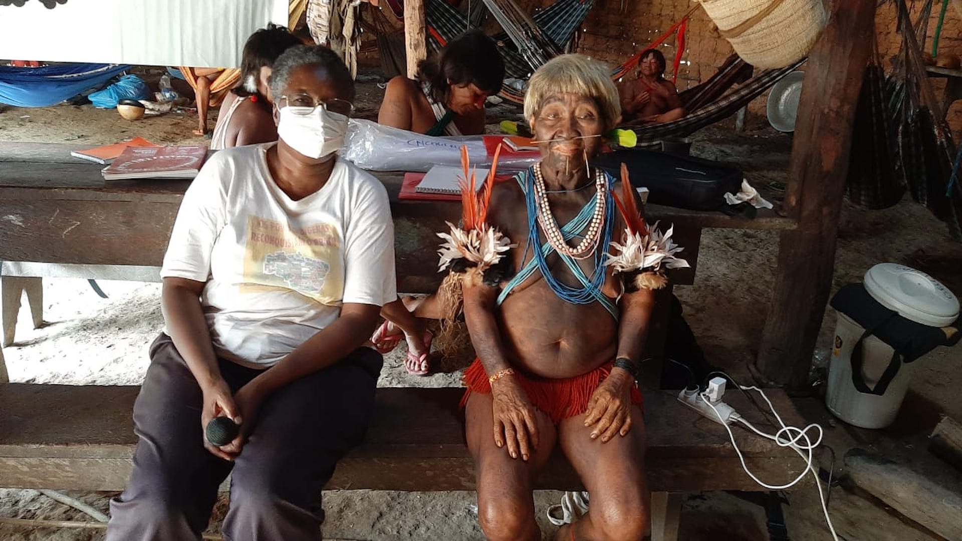 Sr. Mary Agnes Mwangi, of the Consolata Missionary Sisters, sits on a bench next to a member of the Yanomami Tribe. 