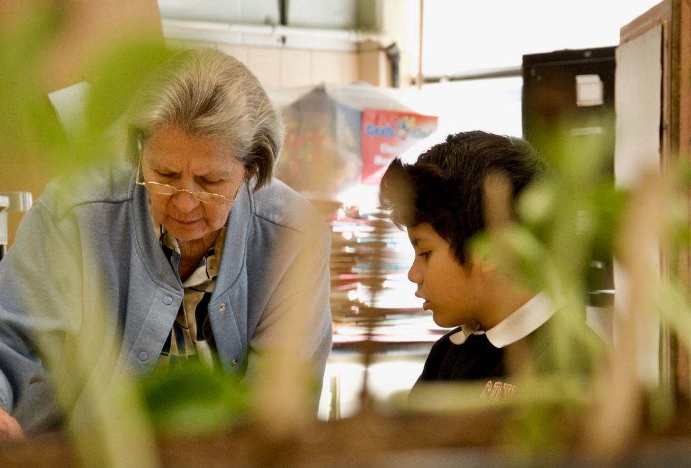 Mercy Sr. Joan Serda works with kindergartner Max on March 16 at St. Pius X Catholic School in Mobile, Alabama. The two are seen through bean-plant seedlings students are growing in the classroom. (GSR photo/Dan Stockman)