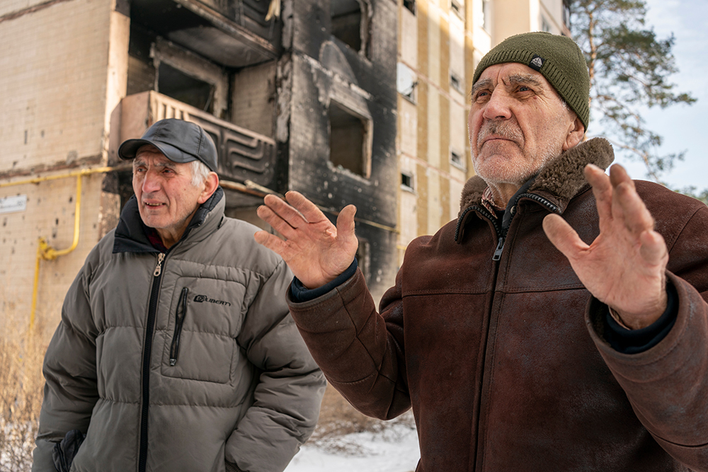 Basil y Nicolai Knutarev frente al edificio de apartamentos de Basil en Irpin, Ucrania, que fue destruido por la artillería rusa en los primeros días de la invasión. El apartamento de Nicolai, al otro lado del estacionamiento, también quedó arrasado.