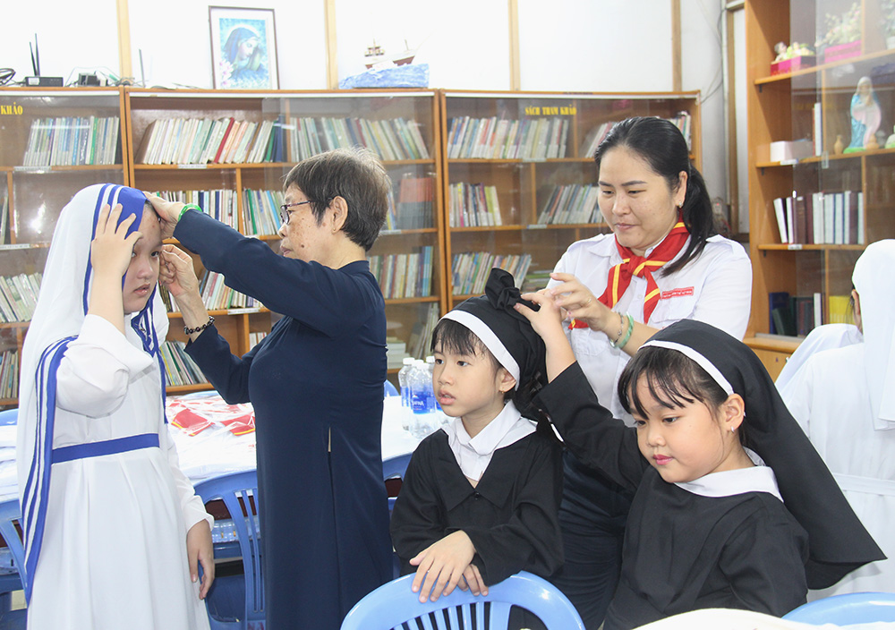 Mary Nguyen Thu Hieu (in dark blue) and another catechist help children put on various habits to introduce 10 orders at Nam Hoa Church in Ho Chi Minh City, Vietnam, April 30. Hieu, 82, who works as a catechist, said, "The show aims at sowing seeds of religious vocations to local young people. The parish produces many religious and priests who wore habits to introduce religious life when they were children." (Joachim Pham)