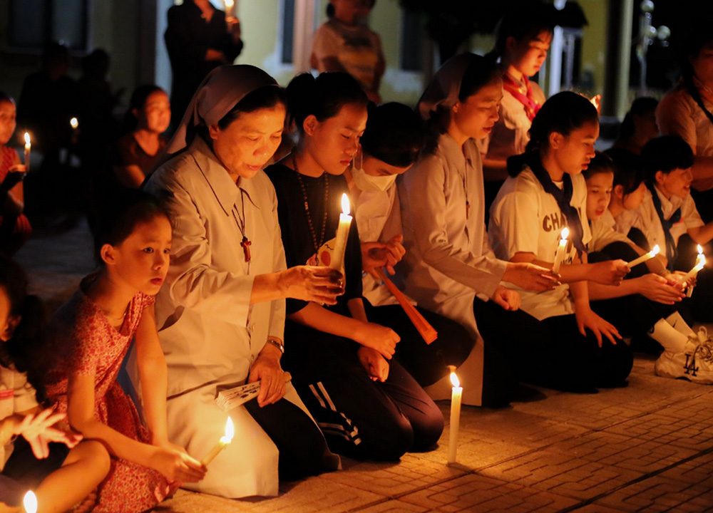 Filles de Marie Immaculée Srs. Mary Vu Thi Thuy Anh (left) and Mary Elizabeth Tran Thi Bich Diep (middle in gray), and other women with candles in hand attend a Eucharist adoration at Xuan Thien Parish in Hue, Vietnam, to pray for more and more young people to answer God's vocational call. (Joachim Pham)