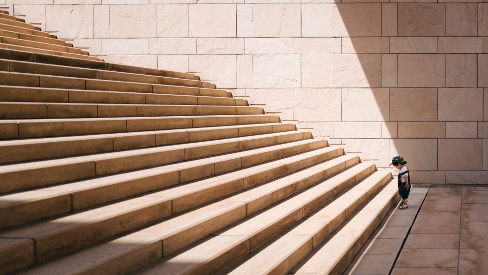 A small child stands at the bottom a large staircase.