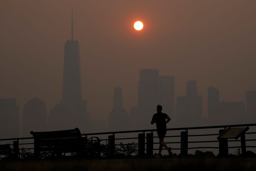 A man runs in front of the sun rising over the lower Manhattan skyline in Jersey City, N.J., on June 8. Intense Canadian wildfires are blanketing the northeastern U.S. 