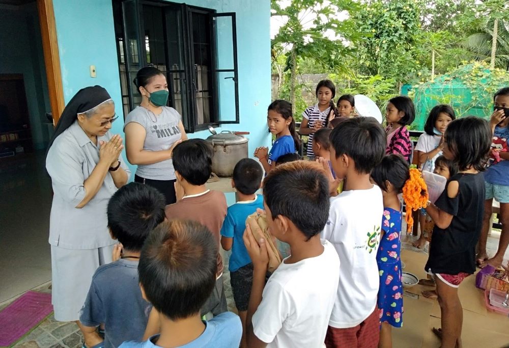 Missionary Benedictine Sr. Edita Eslopor, with the Philberth Foundation scholar volunteer, leads children from a nearby barangay in the Philippines in prayer before their meal. (Courtesy of Edita Eslopor)