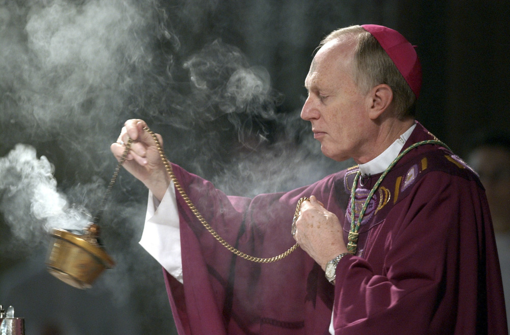 A white man wears a violet zucchetto and purple vestments and swings a thurible