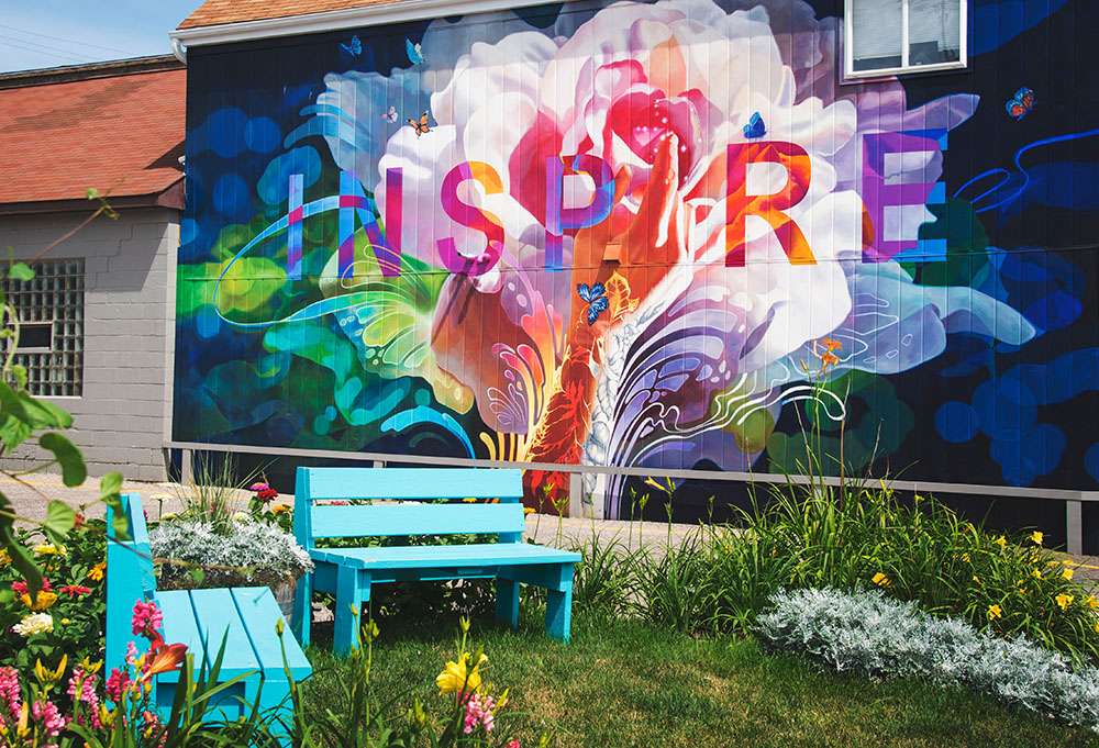 Two blue benches in a garden with a colorful mural that says "Inspire" behind them (Unsplash/Gary Meulemans)