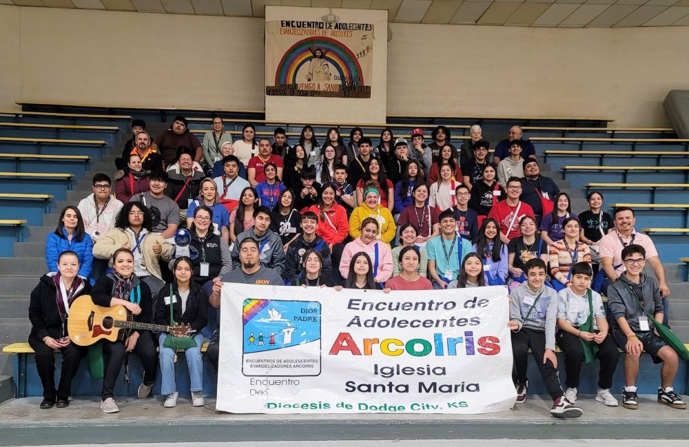 About 50 young people pose on the bleachers and hold a banner for their Arcoiris retreat