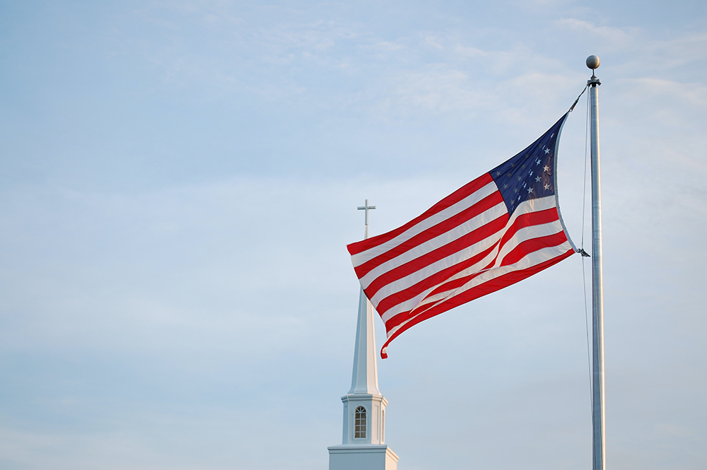 An American flag flies in front of the steeple of a unnamed church (Unsplash/Brad Dodson)