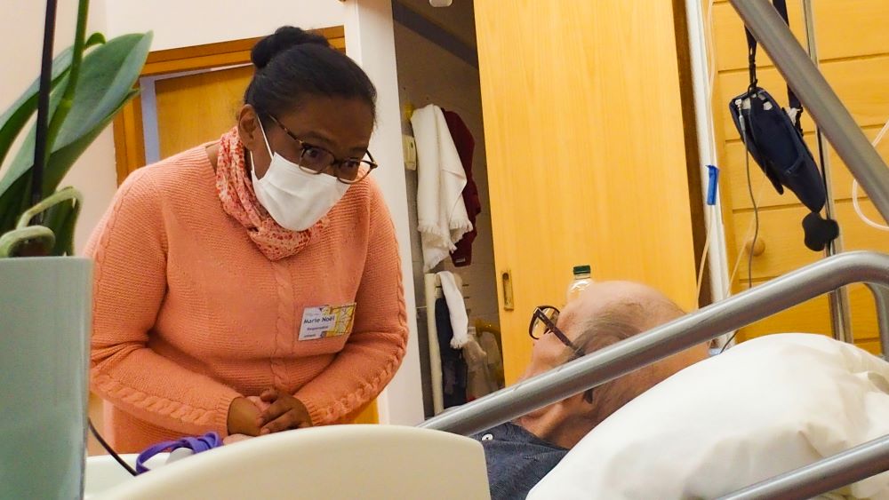 Nurse wearing a mask cares for a patient in hospital bed.