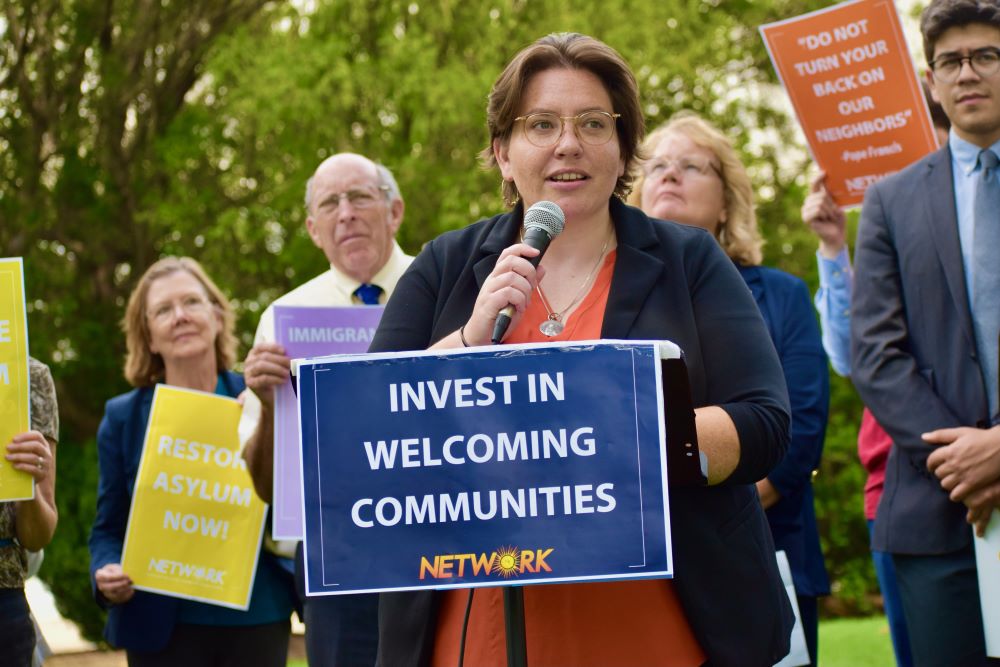 Eilis McCulloh speaks into a microphone in front of sign that reads: "Invest in welcoming communities."