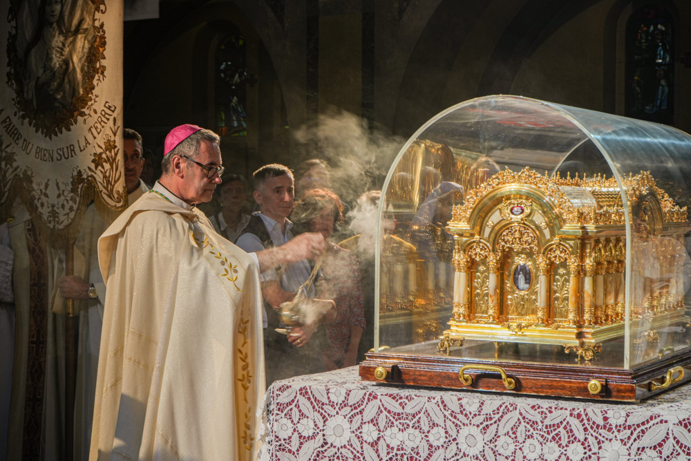 A white man wearing a purple zucchetto and golden vestments swings a thurible towards a gold container