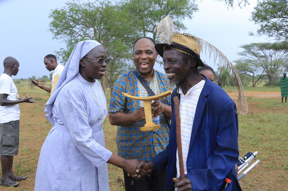 Sr. Mary Lilly Driciru of the Missionary Sisters of Mary Mother of the Church shakes hands with a Karamojong elder who helped coordinate Africa Faith and Justice Network and the local community, as Dominican Fr. Aniedi Okure holds a stool, a symbol of authority gifted to the network. (Courtesy of Mary Lilly Driciru)