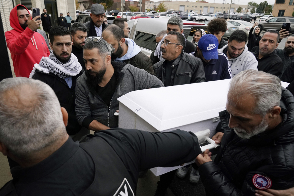 A group of brown men surround and hold an small white casket in a parking lot