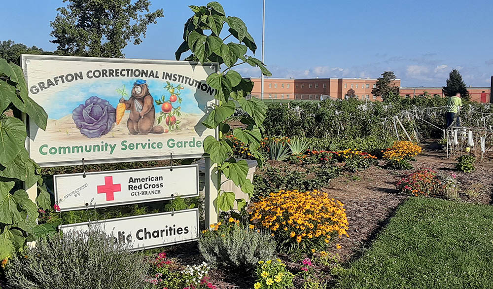 A sign announces the collaborative effort among the inmates and staff at the Grafton Correctional Institution with the American Red Cross and Catholic Charities of the Cleveland Diocese. The men grow a variety of vegetables, including tomatoes, cucumbers, peppers, squash, zucchini, eggplant and onions, for Catholic Charities' food pantry and meal programs. (Dennis Sadowski)