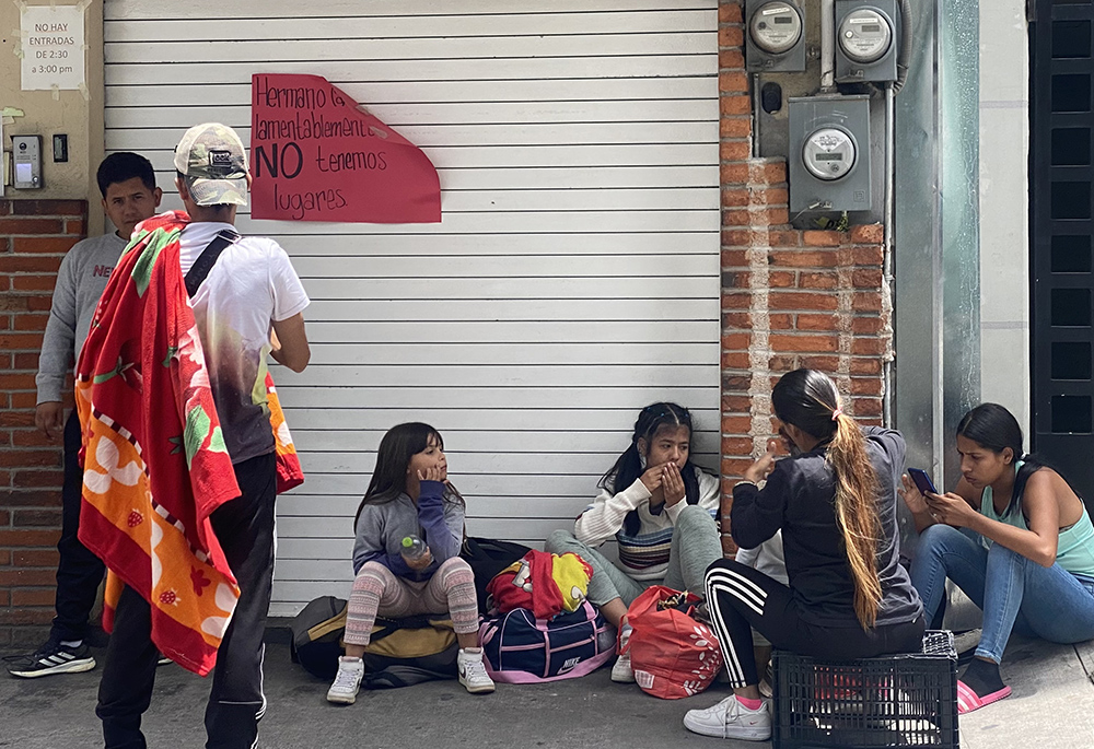 Migrants rest outside the CAFEMIN shelter in Mexico City, Aug. 24, near a sign on the door that says there is no more room inside. With the growing number of migrants heading toward the U.S., shelters along the route from South America to the U.S. southern border are beyond capacity to help. (GSR photo/Rhina Guidos)