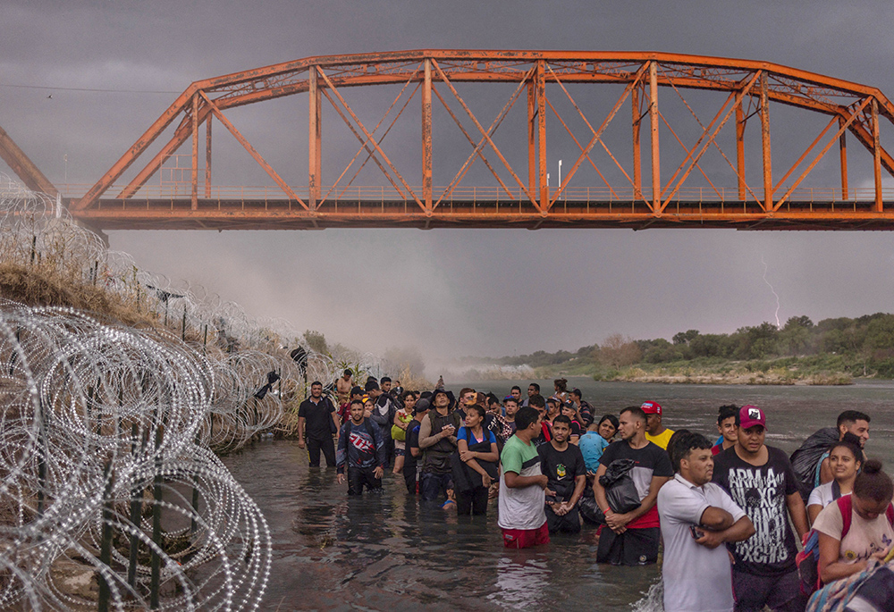 Caen relámpagos y se levanta polvo durante una tormenta eléctrica, el 15 de septiembre, mientras cientos de migrantes hacen cola bajo el Puente Negro, vía del ferrocarril, y esperan a entregarse a las autoridades tras cruzar el Río Grande desde México para entrar en Estados Unidos en Eagle Pass, Texas. (Foto: OSV News/Reuters/Adrees Latif)