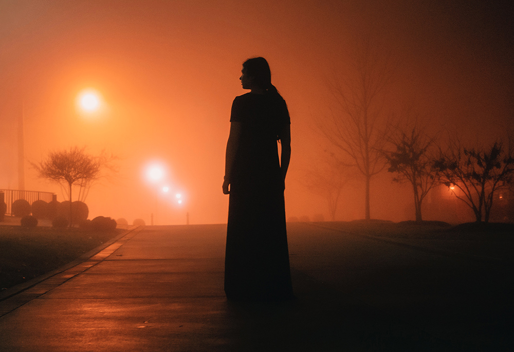 Photo illustration of a woman standing in fog at night (Unsplash/Nik Shuliahin)