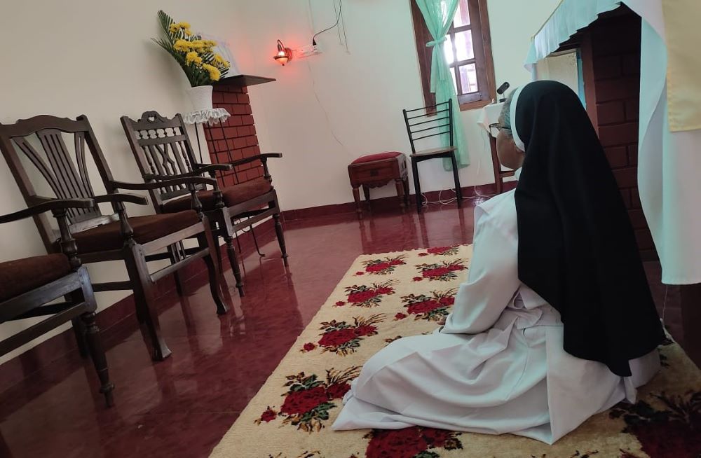 A nun is seen from the back, sitting and praying.