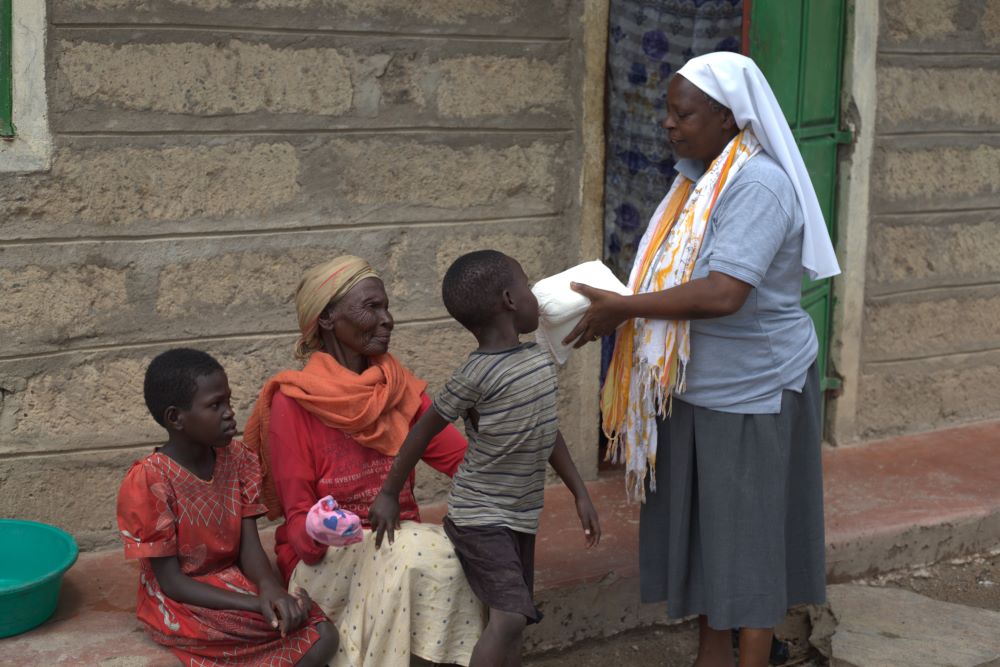 A nun hands a package of flour to woman sitting on a porch with two children.