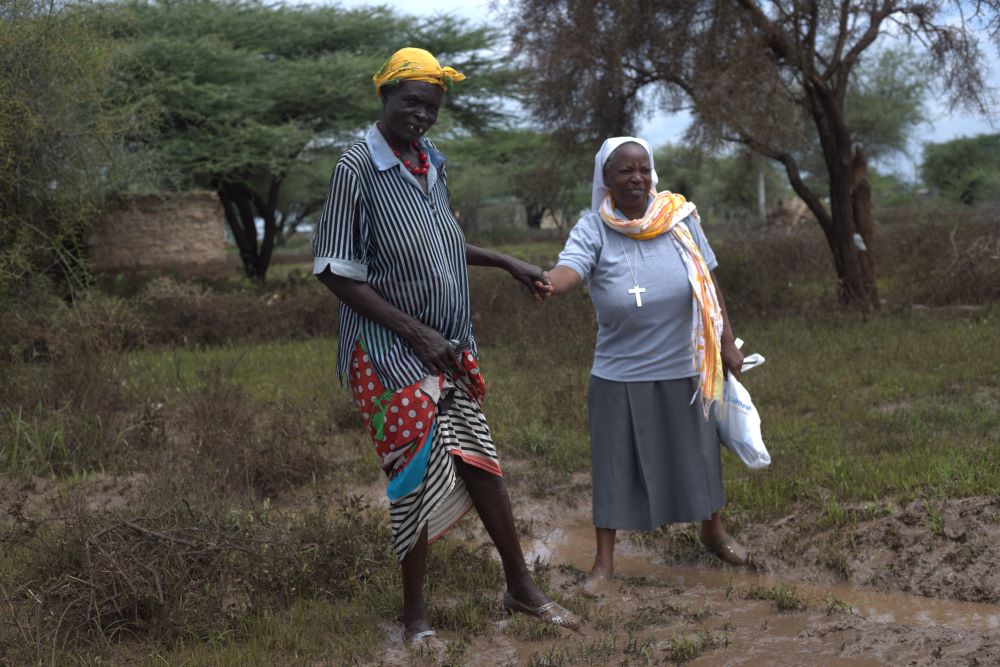 A nun holds the hand of a woman walking through a muddy, wet area.