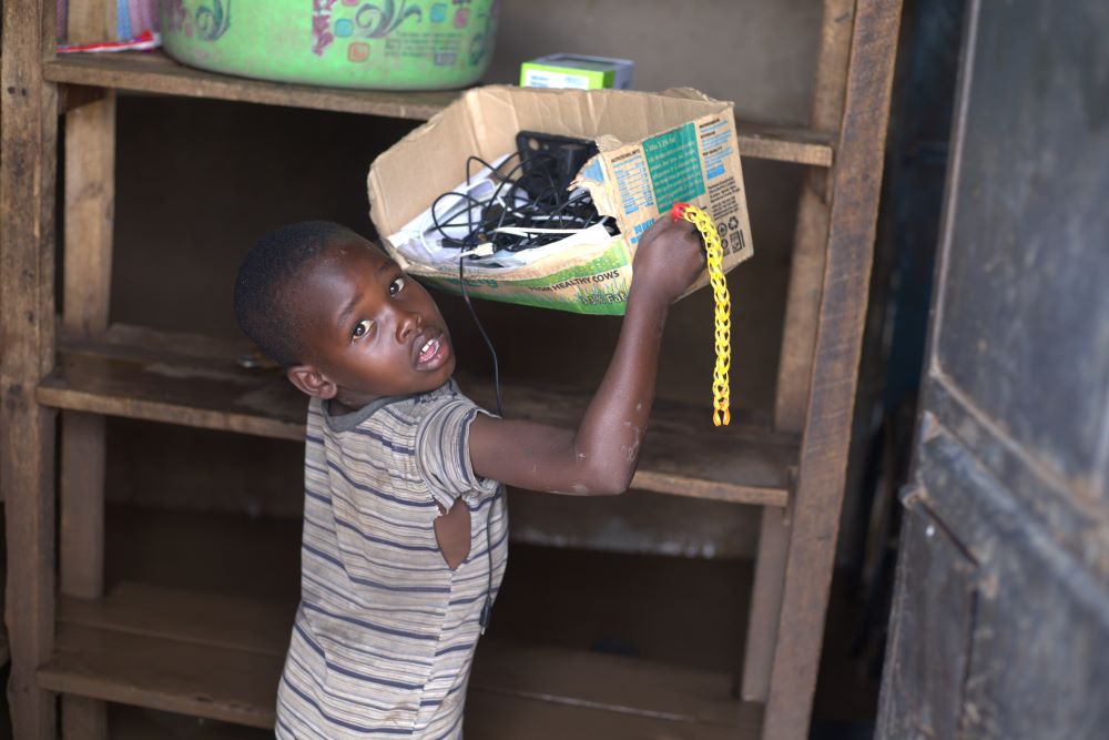 A boy looks at the camera as he lifts a battered box from a shelf.