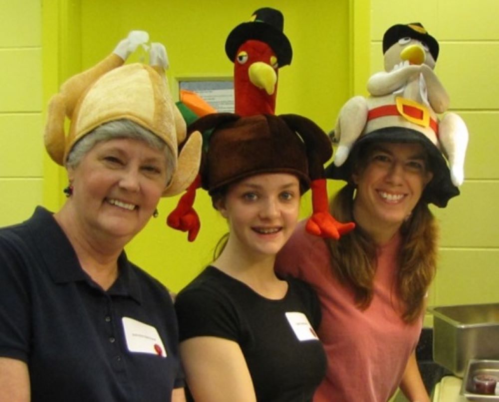 Three women wear hats that look like turkeys.