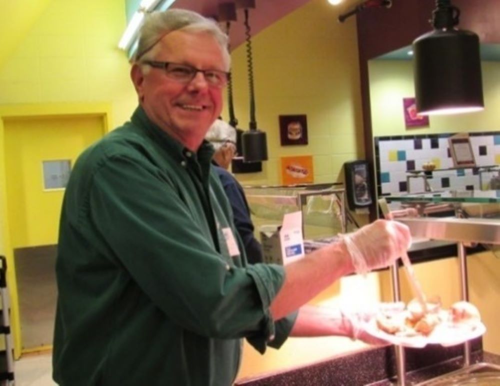 Man stands with plate of food and holds a ladle with gravy.