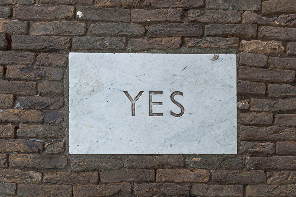 "Yes" carved in a white plaque on a brick wall (Unsplash/Florian Schmetz)