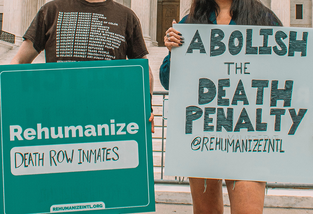 Two people hold signs about rehumanizing death row inmates and abolishing the death penalty (Unsplash/Maria Oswalt)