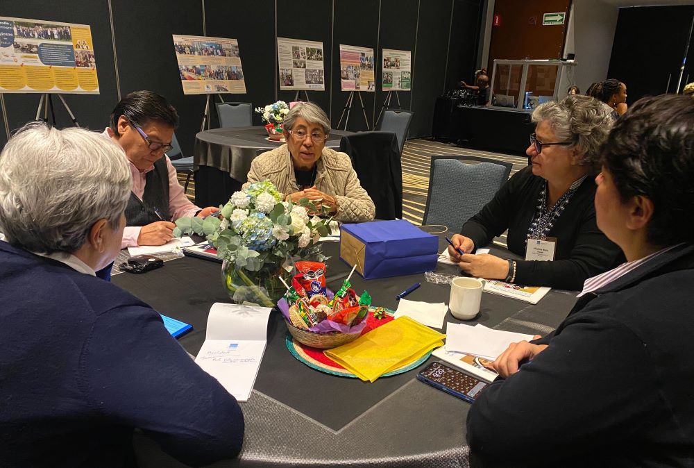 A group of women sit around a table, talking.