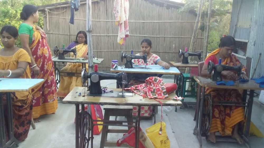 Women sit at tables with sewing machines. 