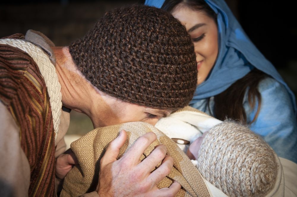 Woman kisses baby while another woman looks on.