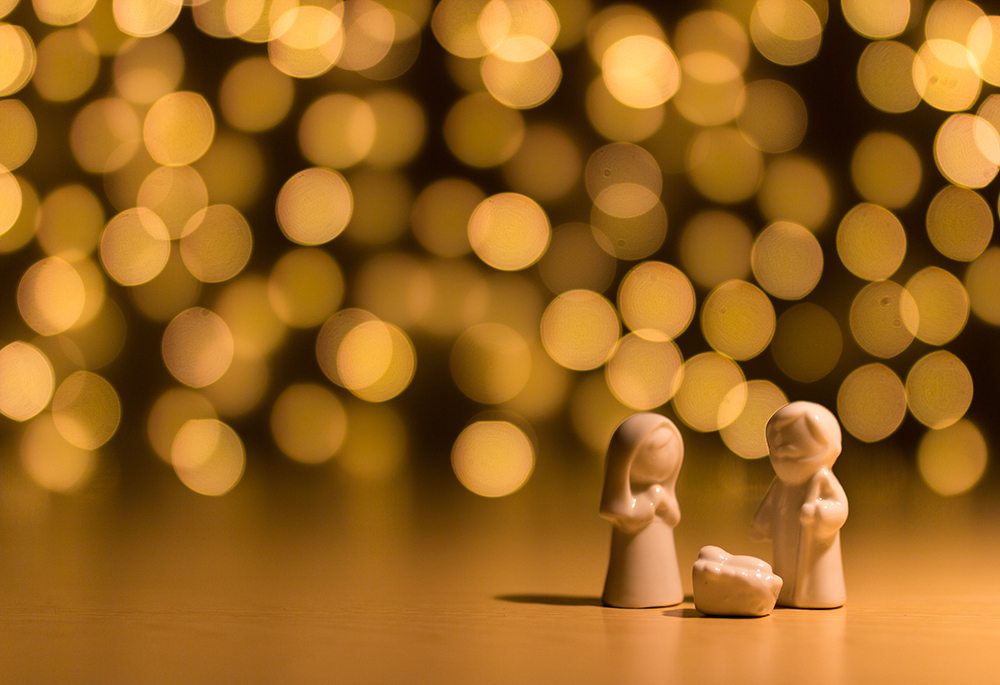 Figurines of Mary, Joseph and baby Jesus are pictured against several shining lights in this photo illustration. (Unsplash/Gareth Harper)