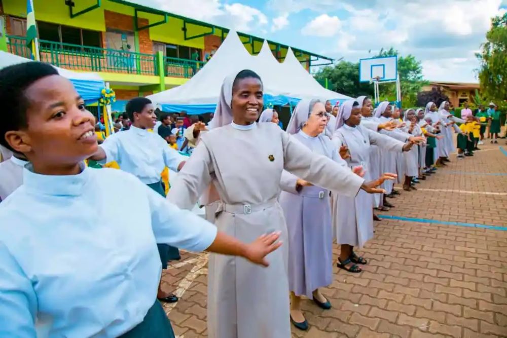 A group of people, most of them nuns wearing white, stand in a line with arms outstretched, 