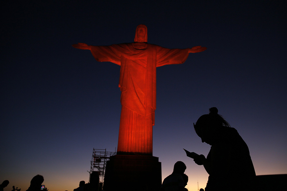 People are pictured in a file photo standing in front of the statue of Christ the Redeemer in Rio de Janeiro as it is lit up in orange to commemorate the Day against Human Trafficking and Missing Persons observed by the Archdiocese of Rio de Janeiro. (OSV News/Reuters/Pilar Olivares)