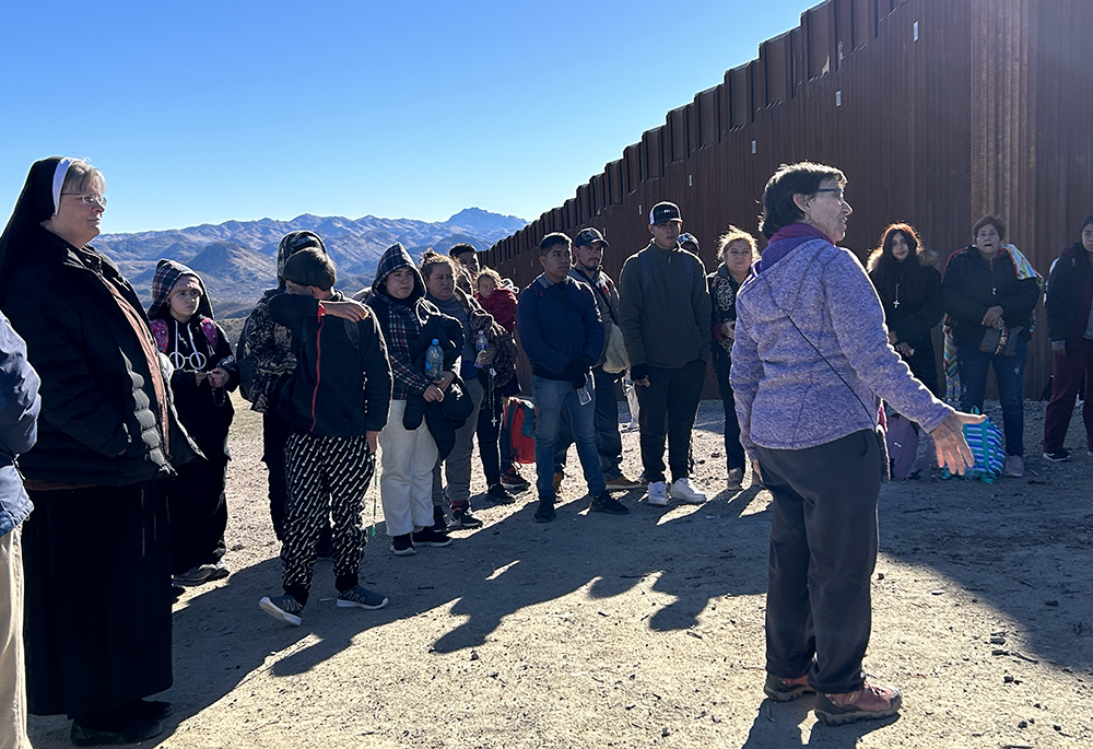 Sr. Judy  Bourg (purple jacket) stands with asylum-seekers who entered the United States through an opening in the U.S.-Mexico border wall. Bourg welcomed each of them, then gathered them in a circle, and said, "We are happy that you are here." To Bourg's left is Sr. Maria Louis Edwards. (Peter Tran)